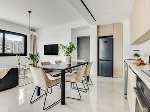 A modern kitchen with a large refrigerator, a dining area with a glass table, and a view of the city through a large window. - Sanders Premier Downtown - Full Building (Limassol)
