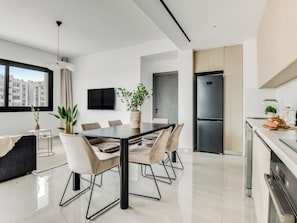 A modern kitchen with a large refrigerator, a dining area with a glass table, and a view of the city through a large window. - Sanders Premier Downtown - Full Building (Limassol)