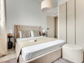 A neatly arranged bedroom with a large bed, bedside lamps, a bedside table, a reading light, and a wardrobe. - Sanders Premier Downtown - Full Building (Limassol)