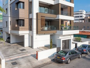 A modern multi-story residential building with balconies, a gated entrance, and parked cars. - Sanders Premier Downtown - Full Building (Limassol)