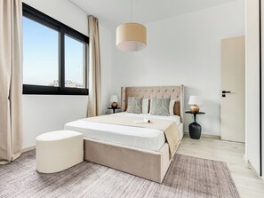 A modern bedroom with a large bed, two bedside tables, a hanging light fixture, and a view of the city through a large window. - Sanders Premier Downtown - Full Building (Limassol)