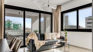 Una sala de estar moderna con un sofá gris, una mesa de centro y vistas de la ciudad a través de amplias ventanas.