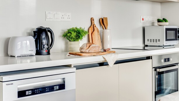 A modern kitchen with a white countertop, a coffee maker, a toaster, a microwave, a bread loaf, a plant, and wooden cutting boards. - Sanders Premier Downtown - Full Building (Limassol)