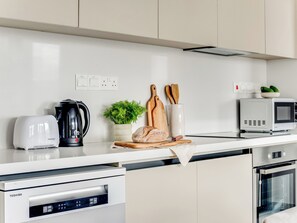 A modern kitchen with a white countertop, a coffee maker, a toaster, a microwave, a bread loaf, a plant, and wooden cutting boards. - Sanders Premier Downtown - Full Building (Limassol)