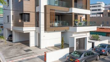 Un edificio residencial moderno de varios pisos, con balcones, una entrada protegida por un portón y coches aparcados.