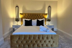 A large bed with a tufted headboard, two bedside lamps, and a folded towel on the bed.