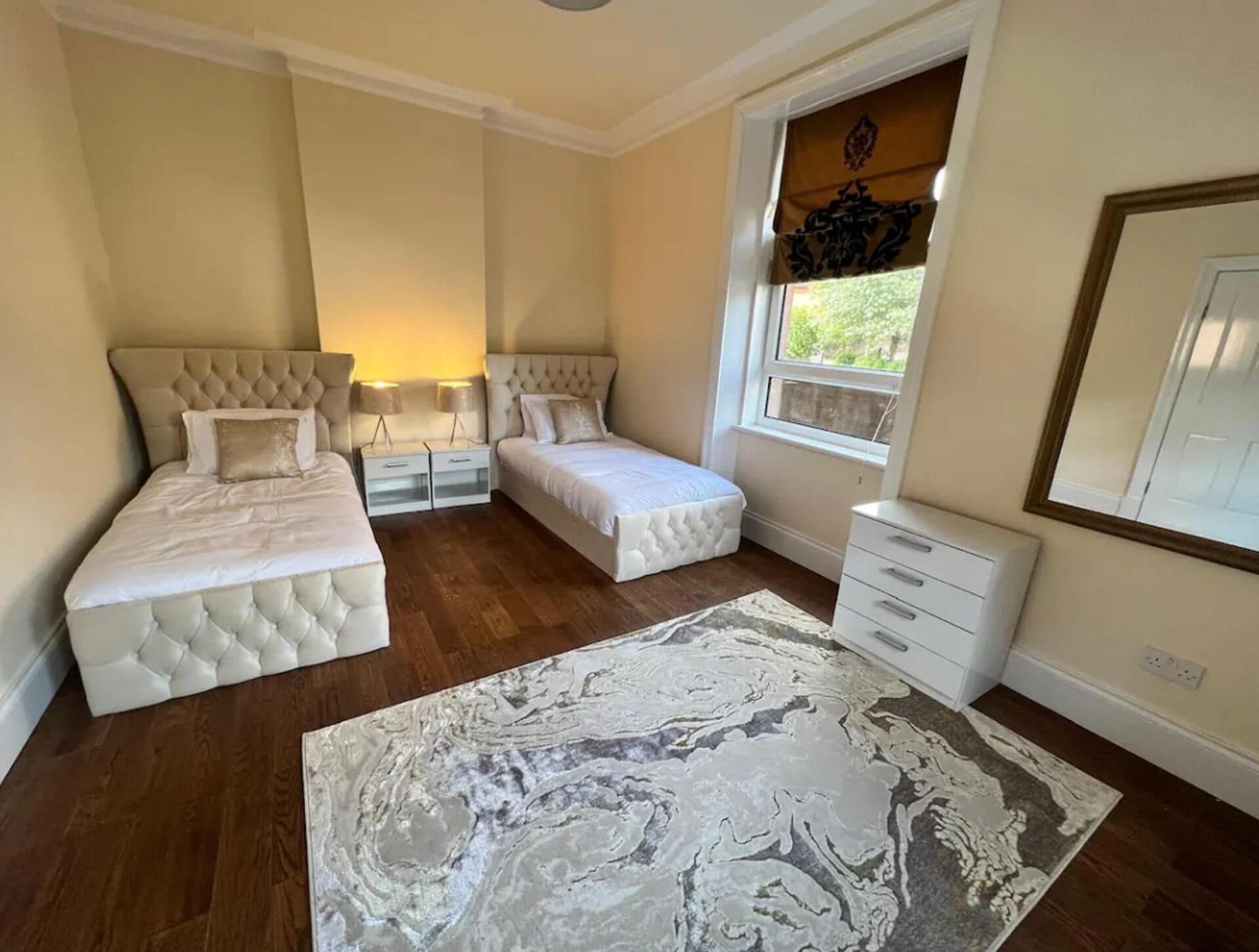 Quarto com duas camas, um tapete grande, uma janela com vista e uma cômoda.