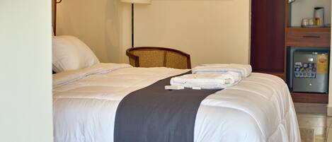 Habitación de hotel con una cama grande, una silla, un cuadro en la pared y un minibar.