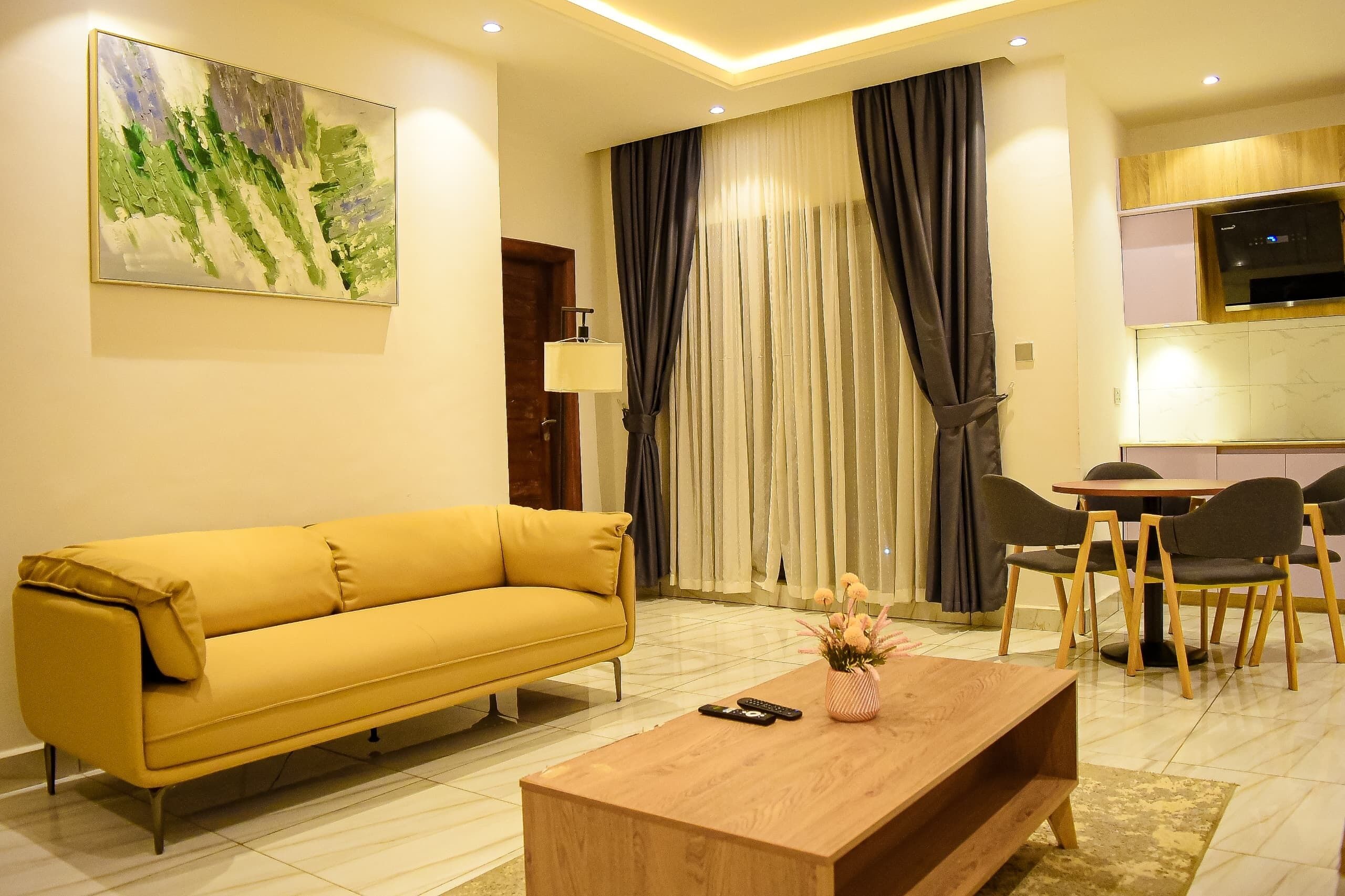 A modern living room with a yellow sofa, a wooden coffee table, and a dining area with chairs and a table.