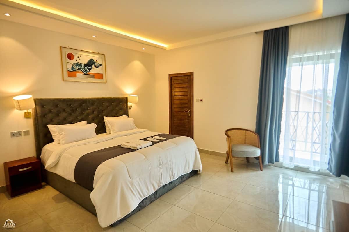 Ein Hotelzimmer mit einem großen Bett, einer Holztür, einem Sessel und einem Fenster mit Vorhängen.