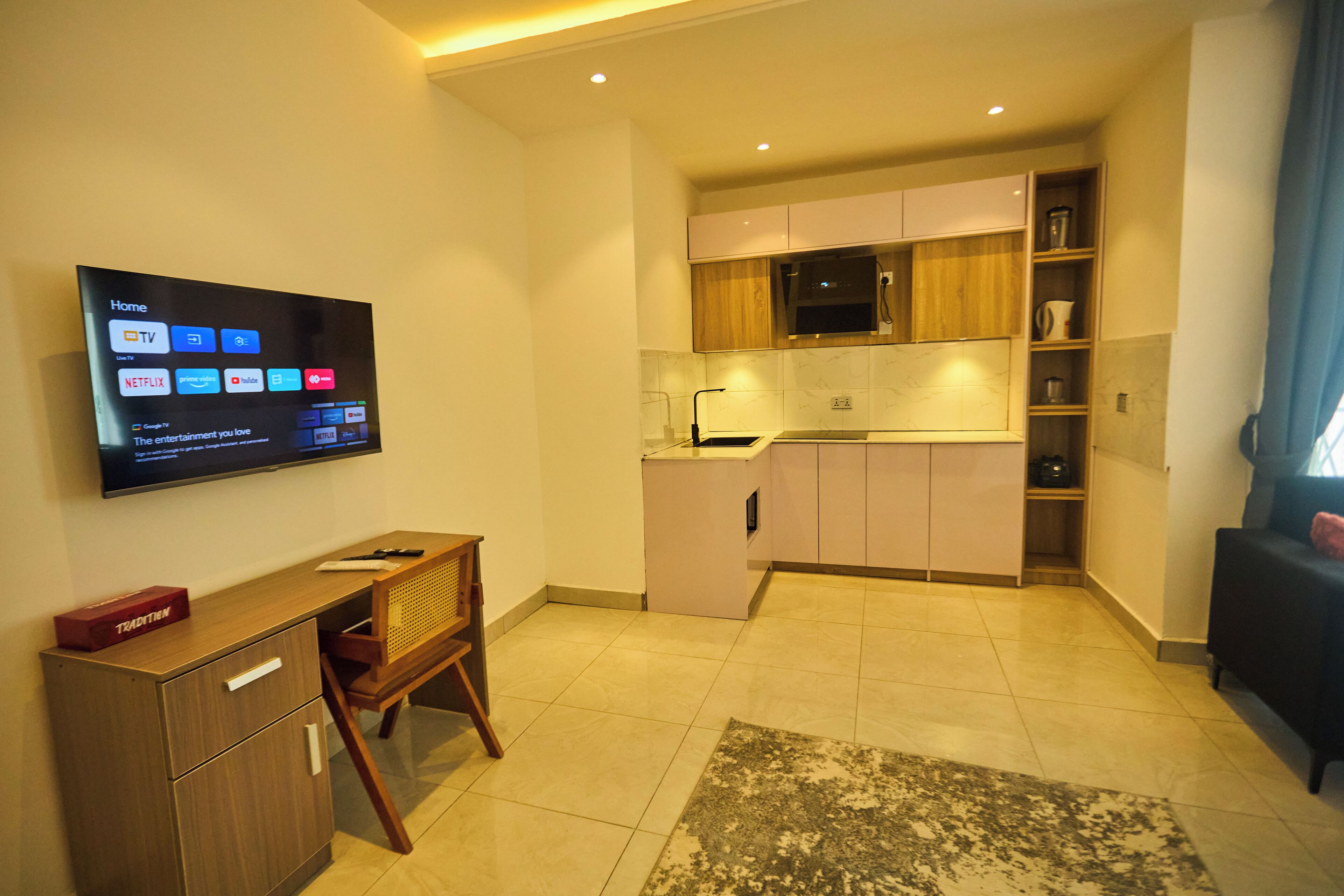 Una cucina moderna con una TV a schermo piatto che mostra servizi di streaming, un tavolo da pranzo in legno e un forno a microonde integrato.