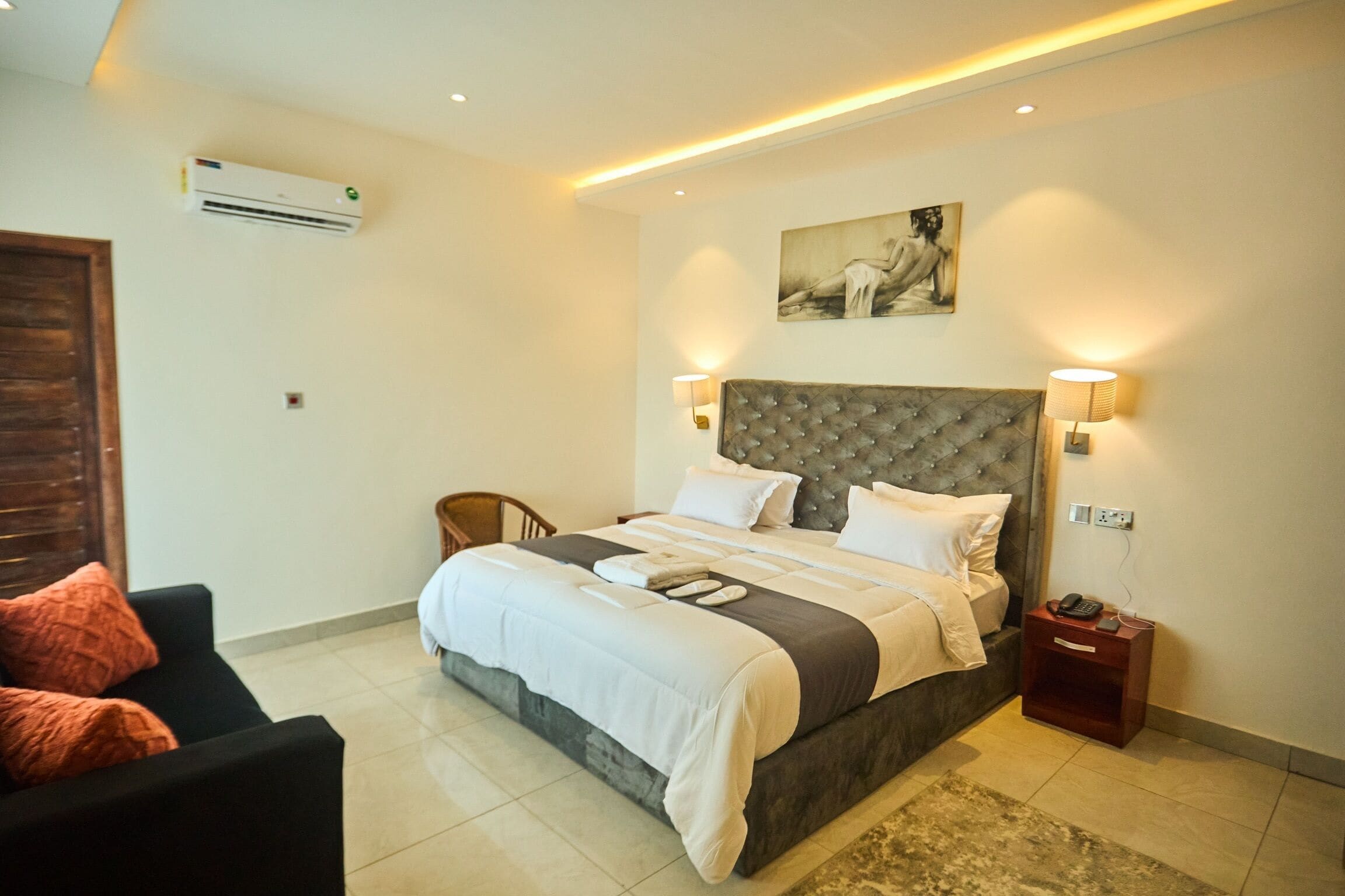 A bedroom with a large bed, bedside lamps, a nightstand, a chair, and a painting on the wall.