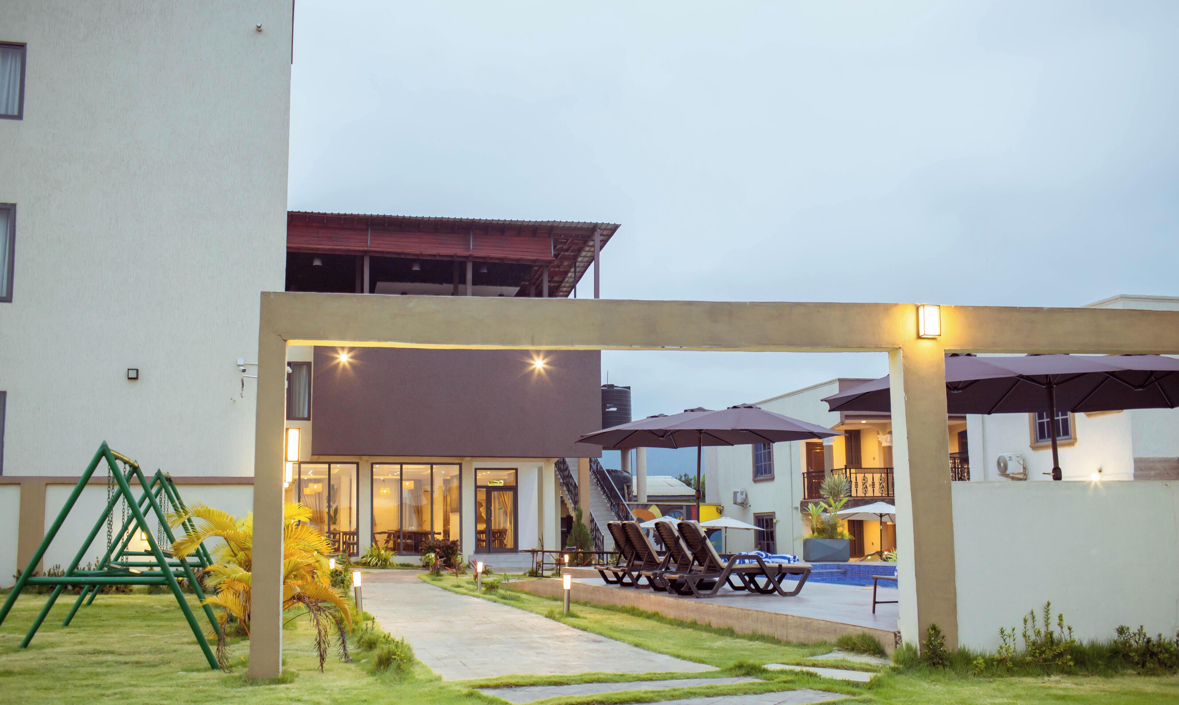 A hotel courtyard with a swing set, lounge chairs, and umbrellas.