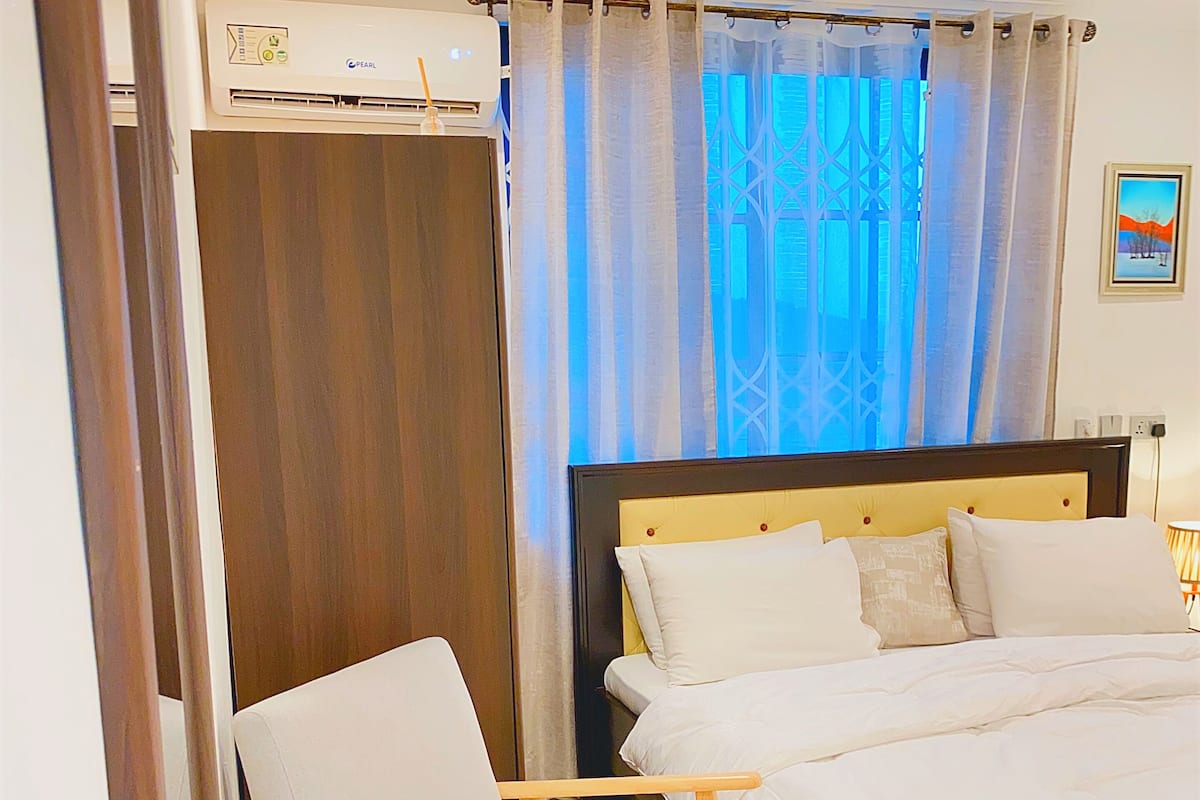 Ein Hotelzimmer mit einem Bett, einem Sessel, einem Fenster mit Vorhängen und einer Klimaanlage.