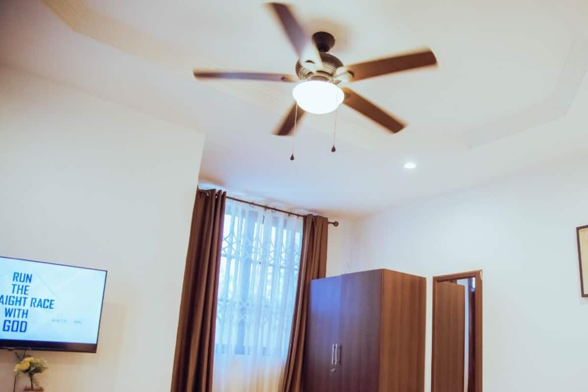 Ein Zimmer mit Deckenventilator, Fernseher mit motivierender Botschaft, Kleiderschrank und einem gerahmten Bild an der Wand.