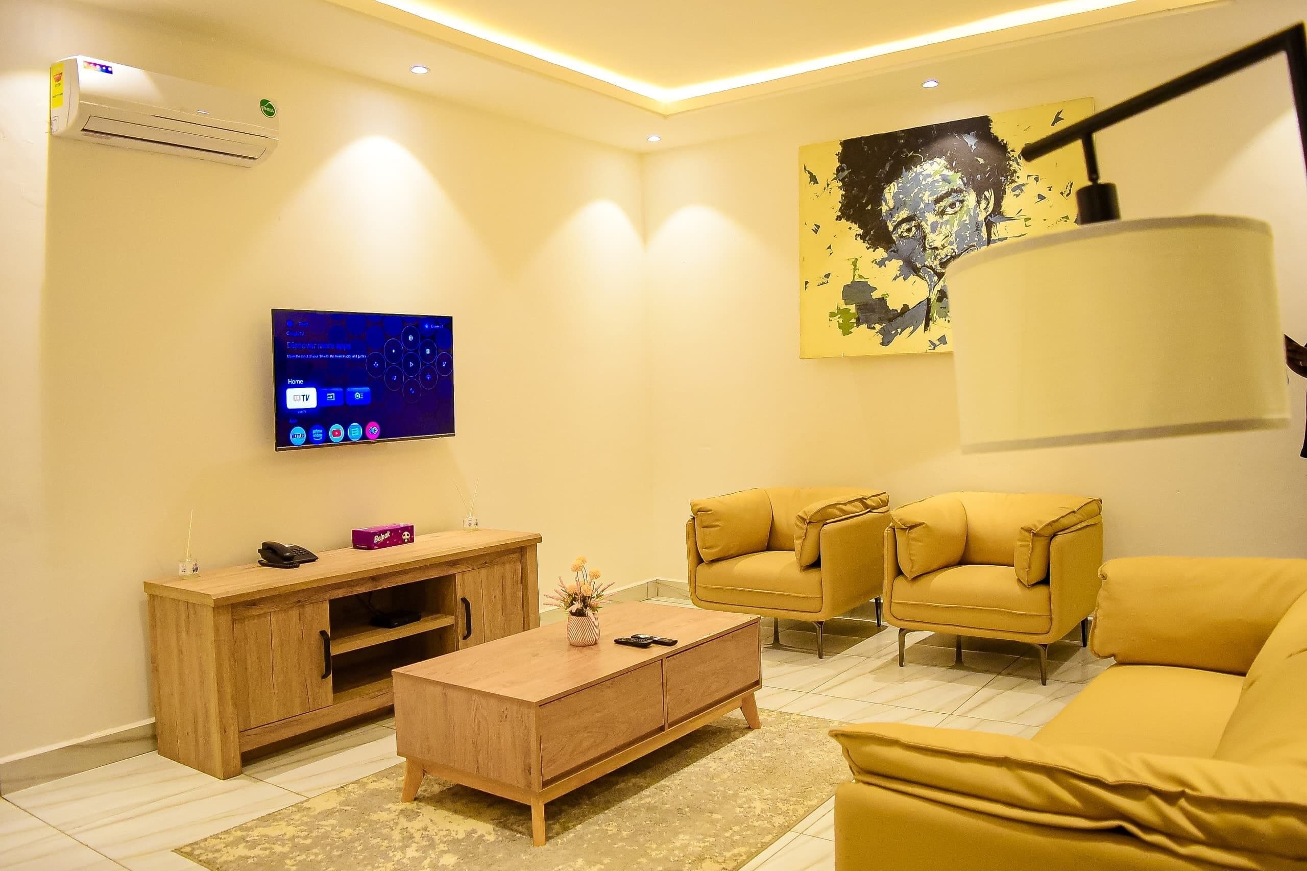 A modern living room with a flat-screen TV, wooden entertainment unit, yellow sofas, and a large abstract painting.