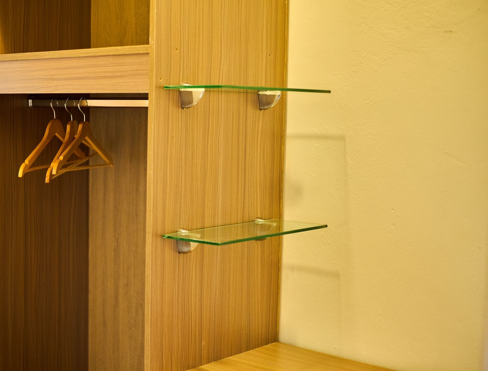 A wooden wardrobe with two glass shelves and a wooden hanger rod.