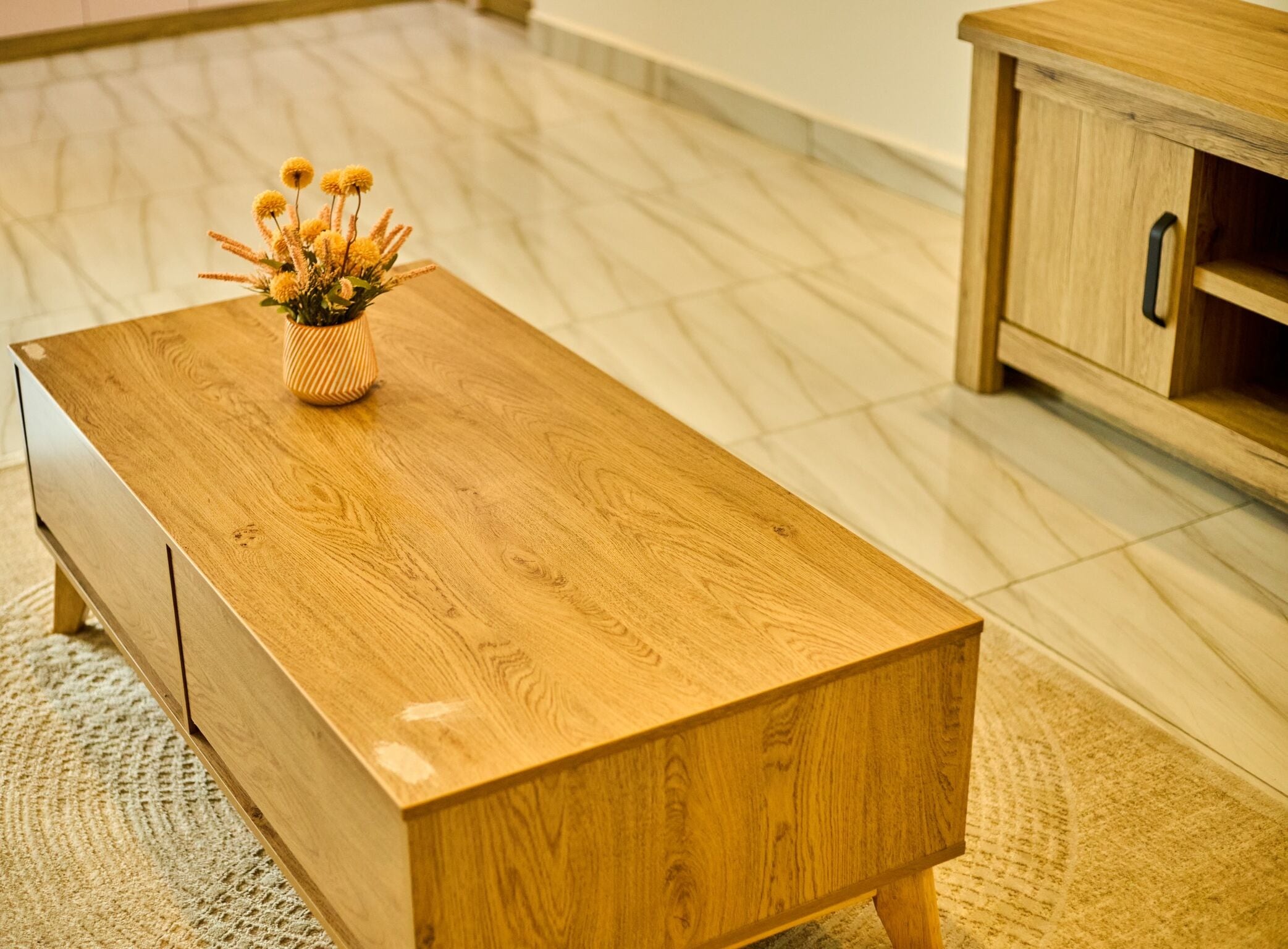 A wooden coffee table with a vase of yellow flowers.