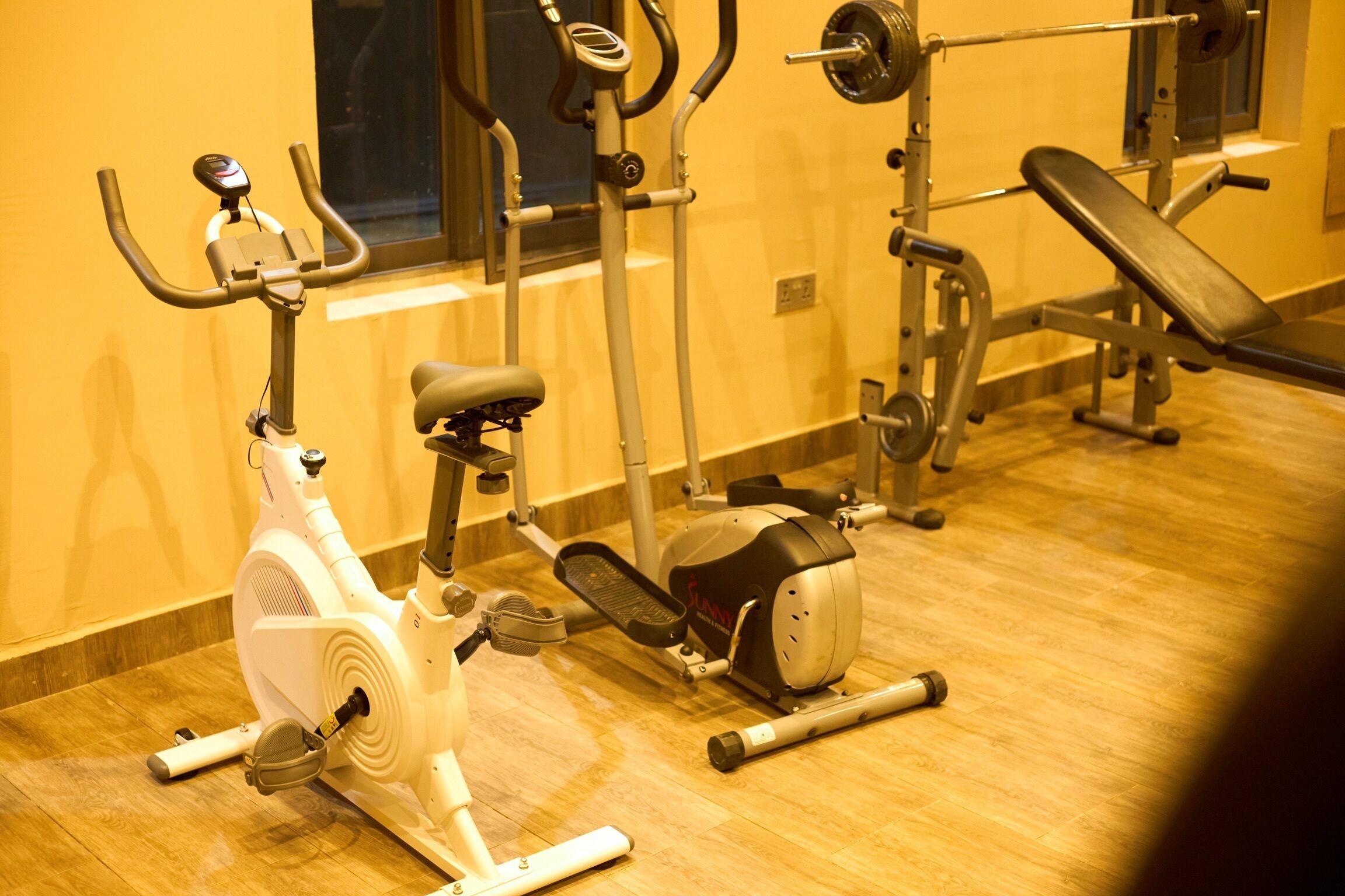 A gym with exercise equipment including an elliptical, a stationary bike, and a bench.