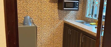 Cocina compacta con salpicadero de azulejos, microondas integrado, armarios de madera oscura y una ventana con barandilla decorativa.