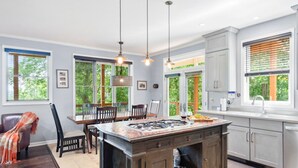 Una cocina moderna con una isla central, iluminación colgante y ventanas amplias con persianas.