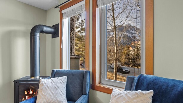 A cozy room with a fireplace, two blue armchairs, and a window with a view of a snowy landscape. - Mountain Views | Outdoor Heated Pool | Hot Tub (Canmore)