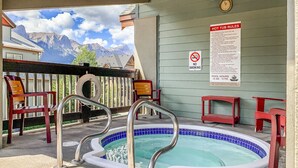 A hot tub with a no smoking sign and pool hours sign, surrounded by red chairs and a mountain view. - Mountain Views | Outdoor Heated Pool | Hot Tub (Canmore)