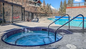 A pool area with a hot tub, a smaller pool, and a stone wall. - Mountain Views | Outdoor Heated Pool | Hot Tub (Canmore)