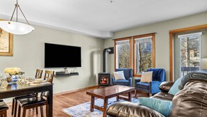 A living room with a fireplace, a dining area, and a TV mounted on the wall. - Mountain Views | Outdoor Heated Pool | Hot Tub (Canmore)