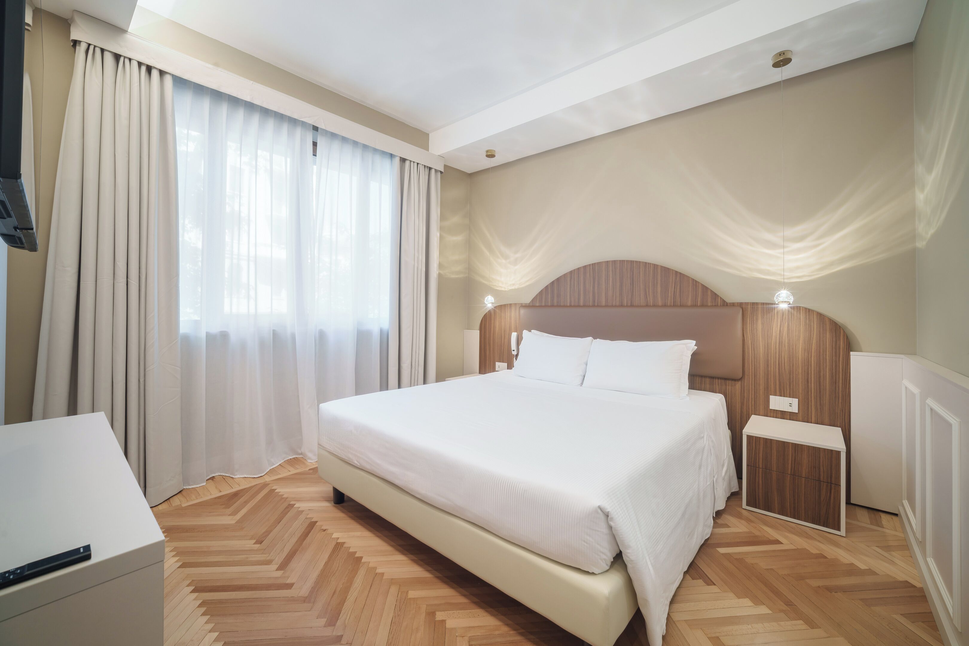 A hotel room with a large bed, a bedside table, a nightstand, and a wooden floor.