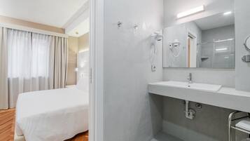 Une chambre d’hôtel moderne dotée d’un grand lit, d’une salle de bain avec douche et d’une coiffeuse avec miroir.