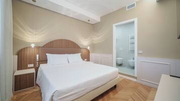 Un dormitorio con una cama grande, mesitas de noche, cabecero de madera, cabina de ducha de vidrio y una puerta blanca.
