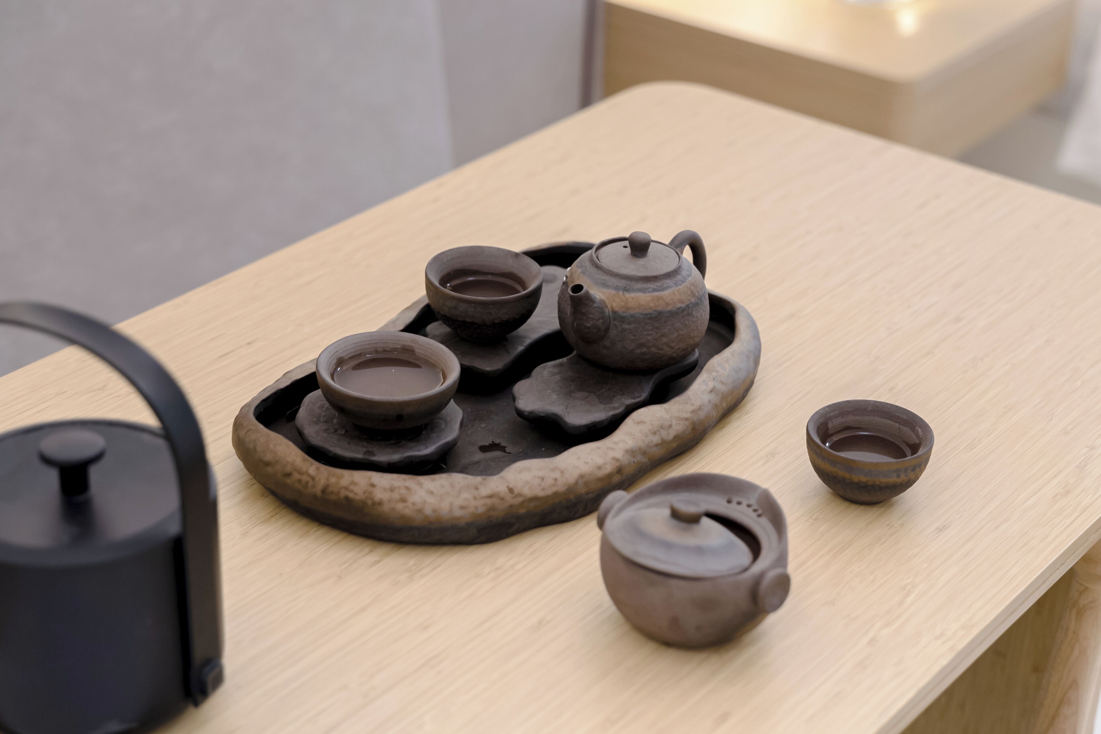 A wooden table with a tea set including a teapot, cups, and a saucer.