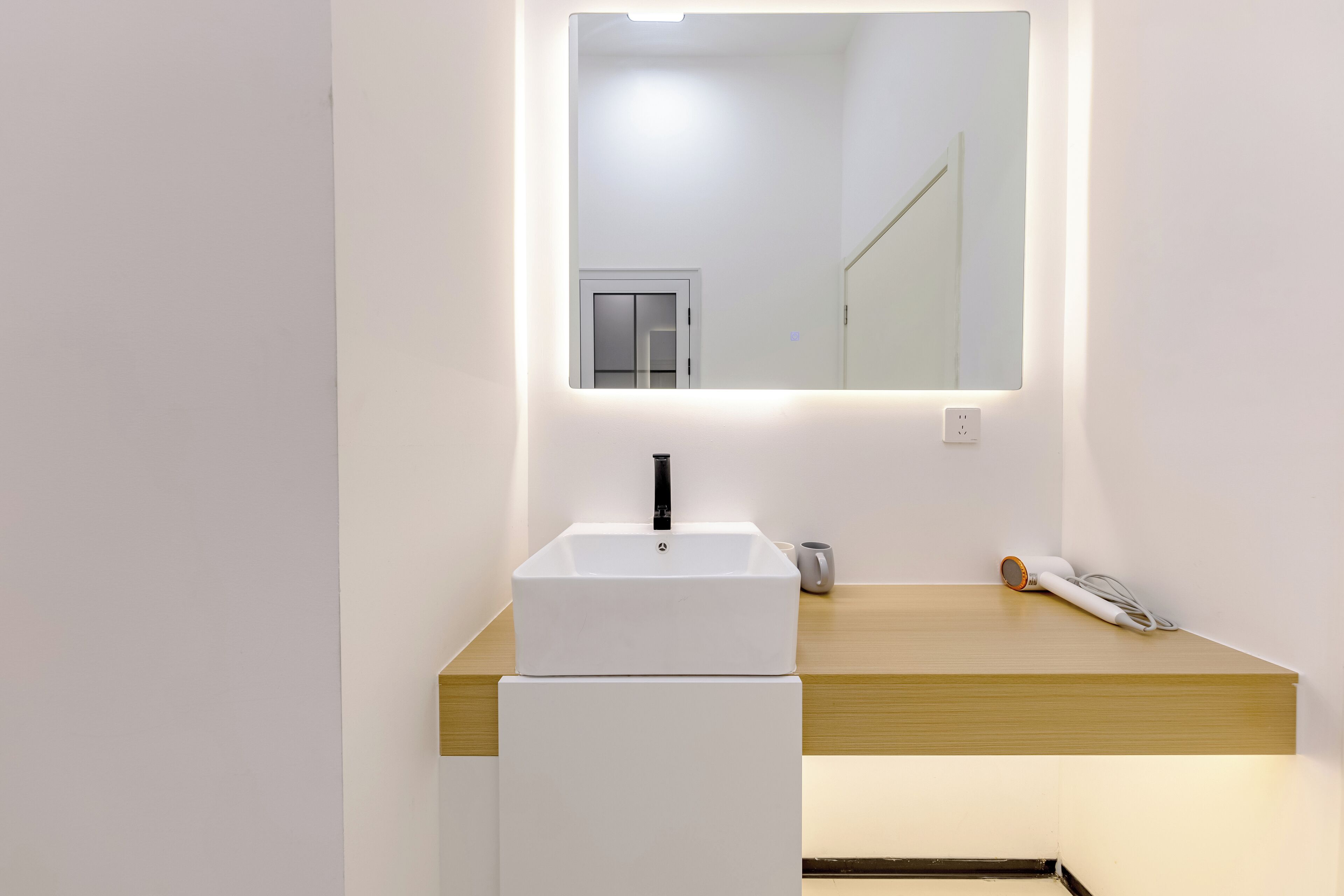 Ein modernes Badezimmer mit einem weißen Waschbecken, einem Spiegel darüber und einer Holzauslage.