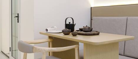A modern room with a wooden table, a chair, a sofa, and a tea set.