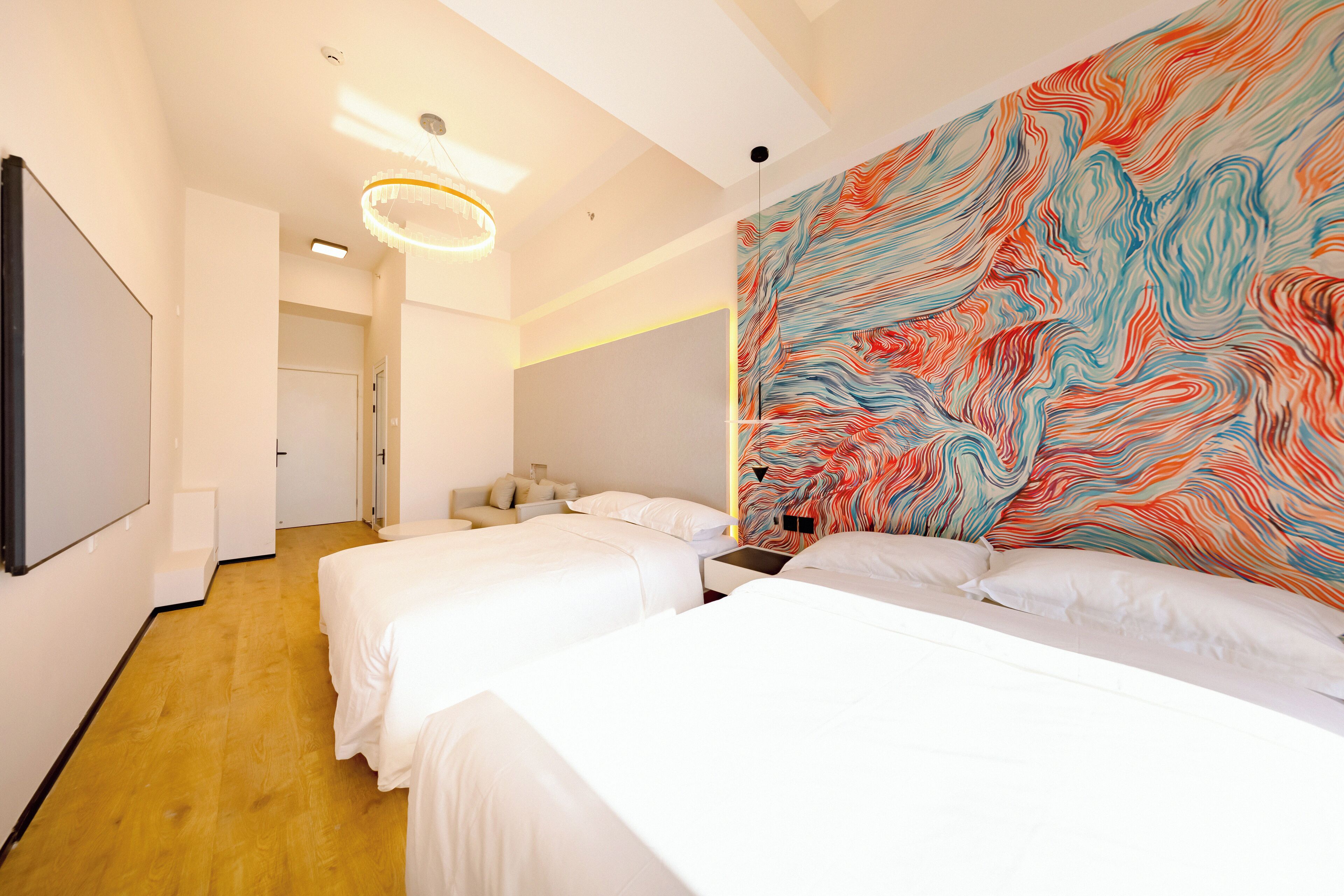 Une chambre d’hôtel avec deux lits, une grande fresque abstraite sur le mur et un lustre moderne.