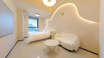 A modern bedroom with a bed, sofa, and round table, featuring a unique wall design and a city view.