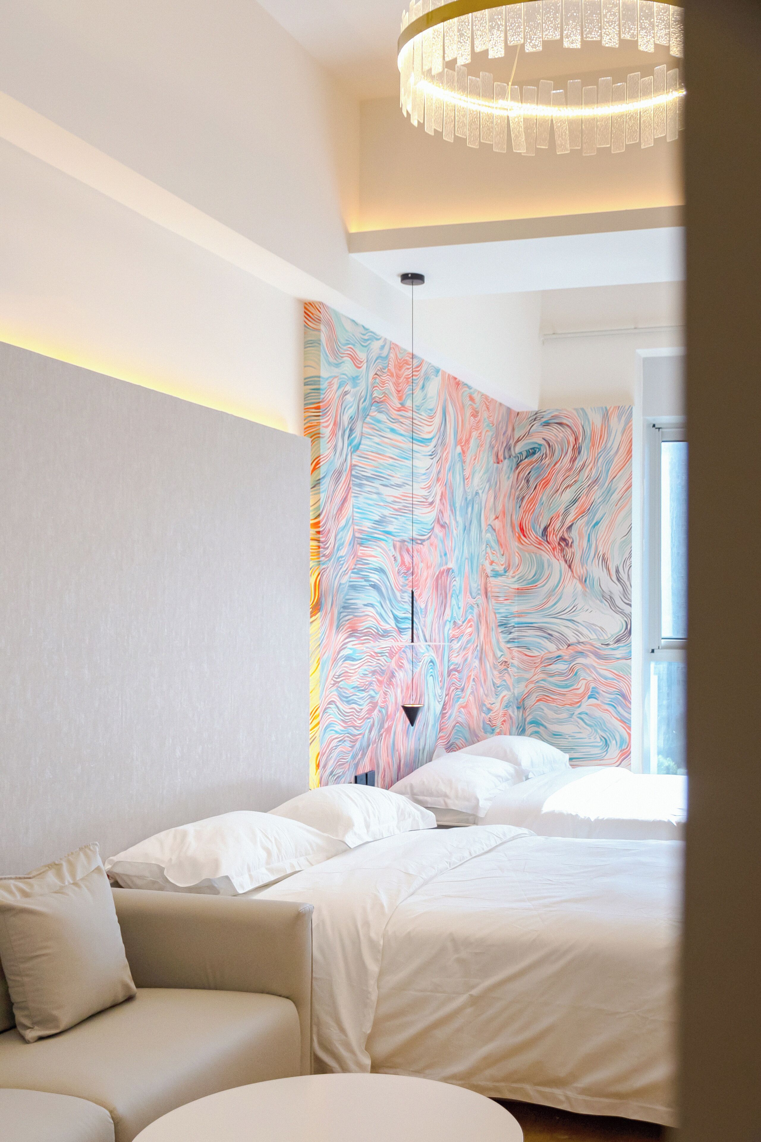 A modern bedroom with a large bed, a sofa, and a colorful abstract mural on the wall.