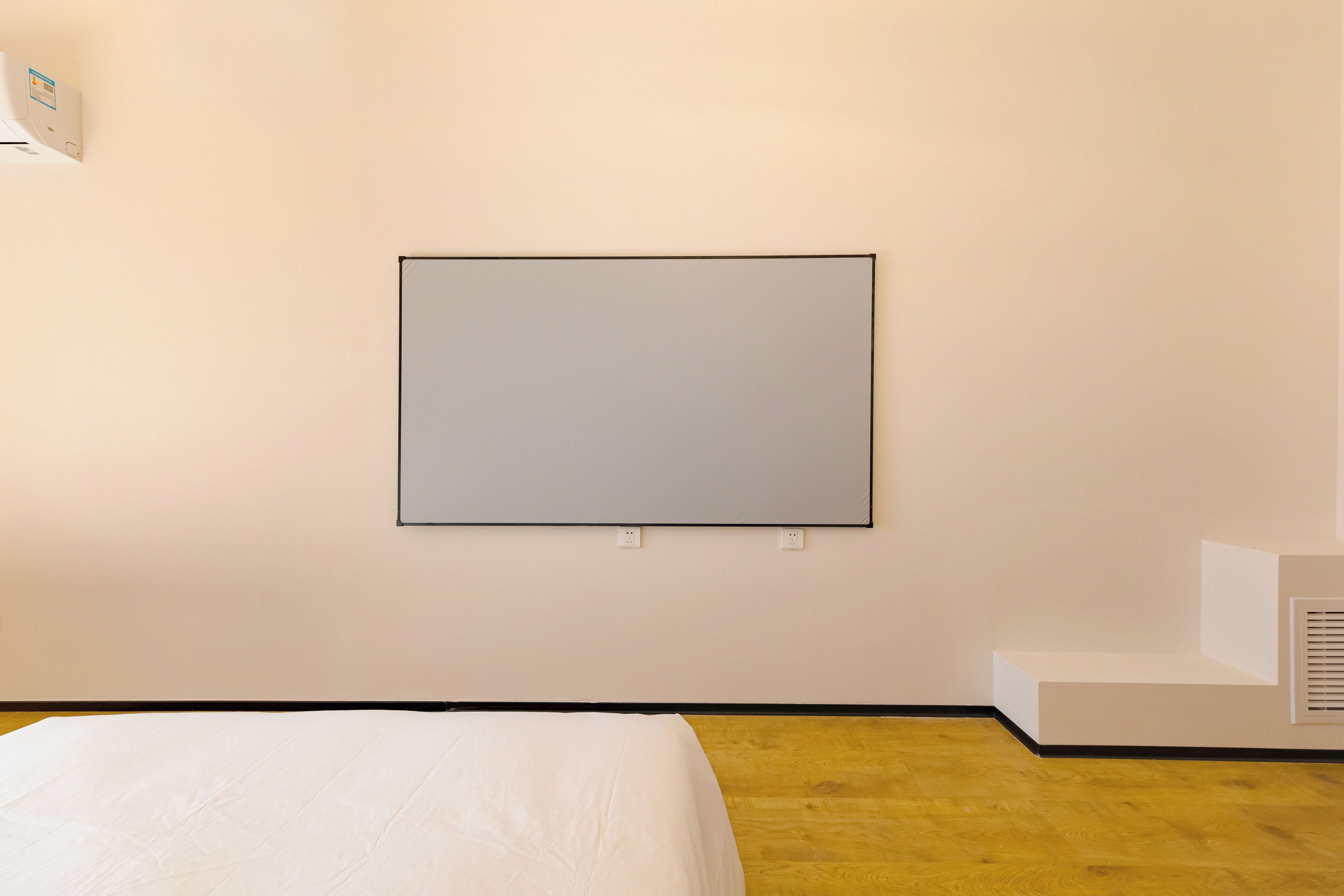A hotel room with a bed, a white wall-mounted TV, and a wooden floor.