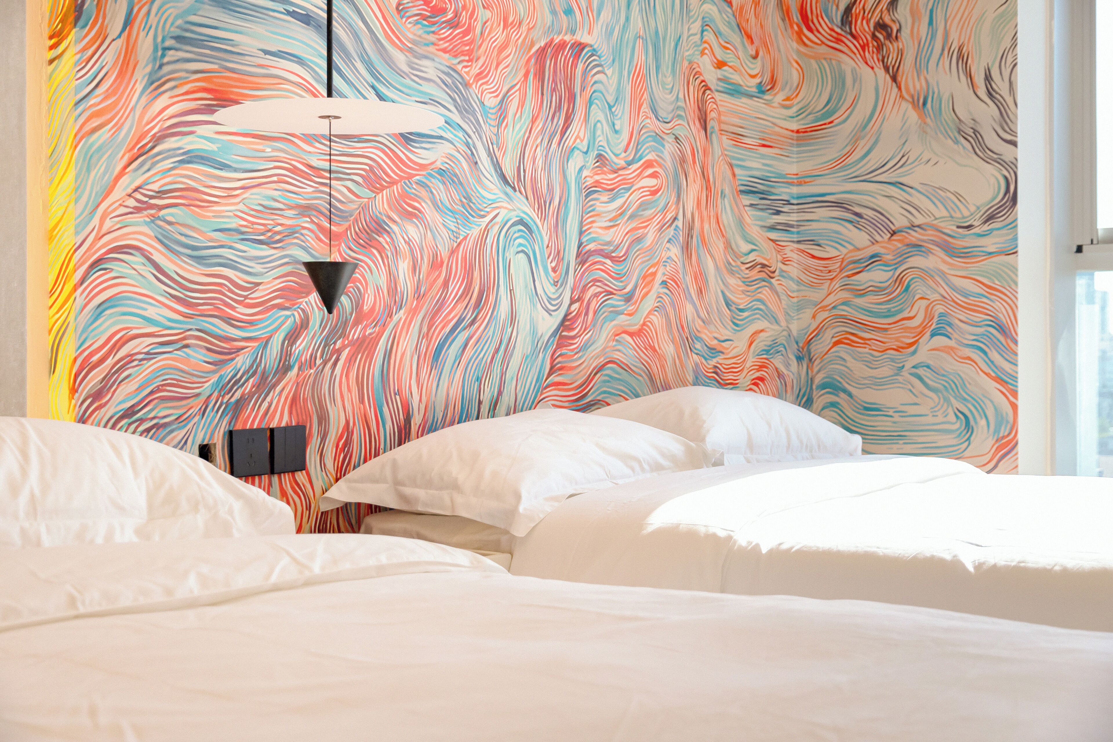 Une chambre d’hôtel avec un lit, des oreillers et un motif mural abstrait aux couleurs vives.