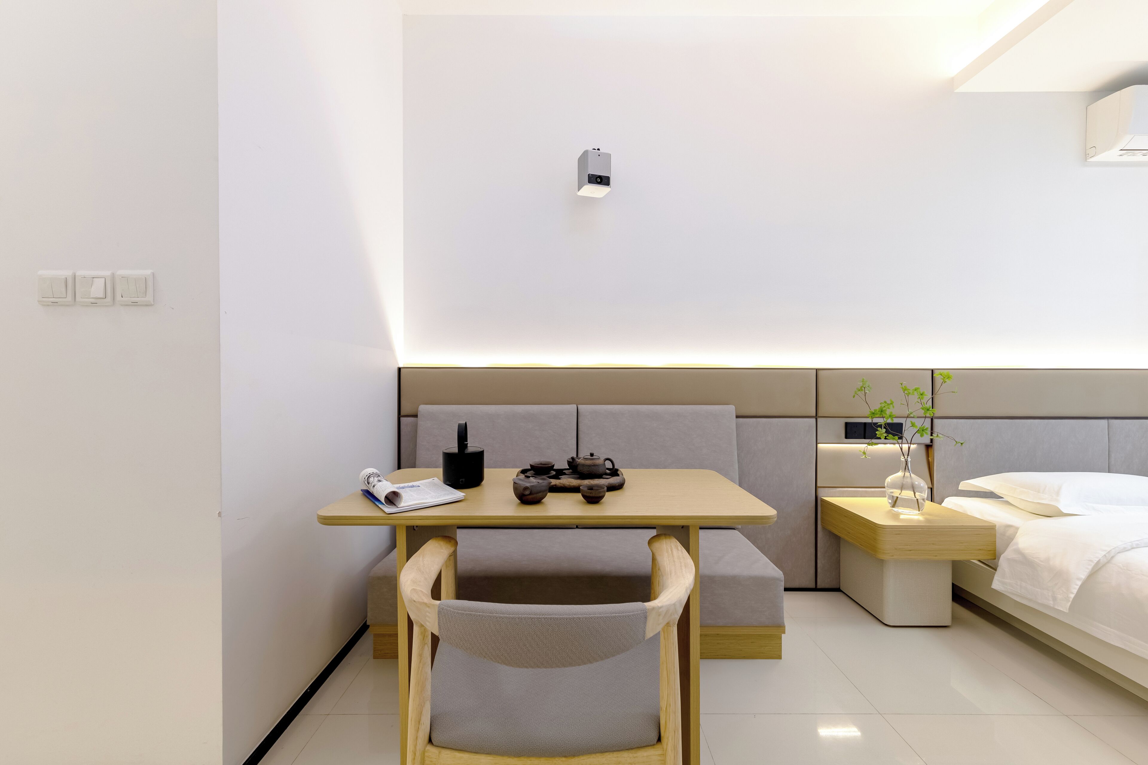 Moderni hotellihuone, jossa on puinen työpöytä, tuoli, yöpöytä maljakolla ja valkoisilla lakanoiden peitetyllä sängyllä.