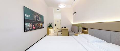 A modern hotel room with a large bed, a desk, and a TV mounted on the wall displaying a movie.