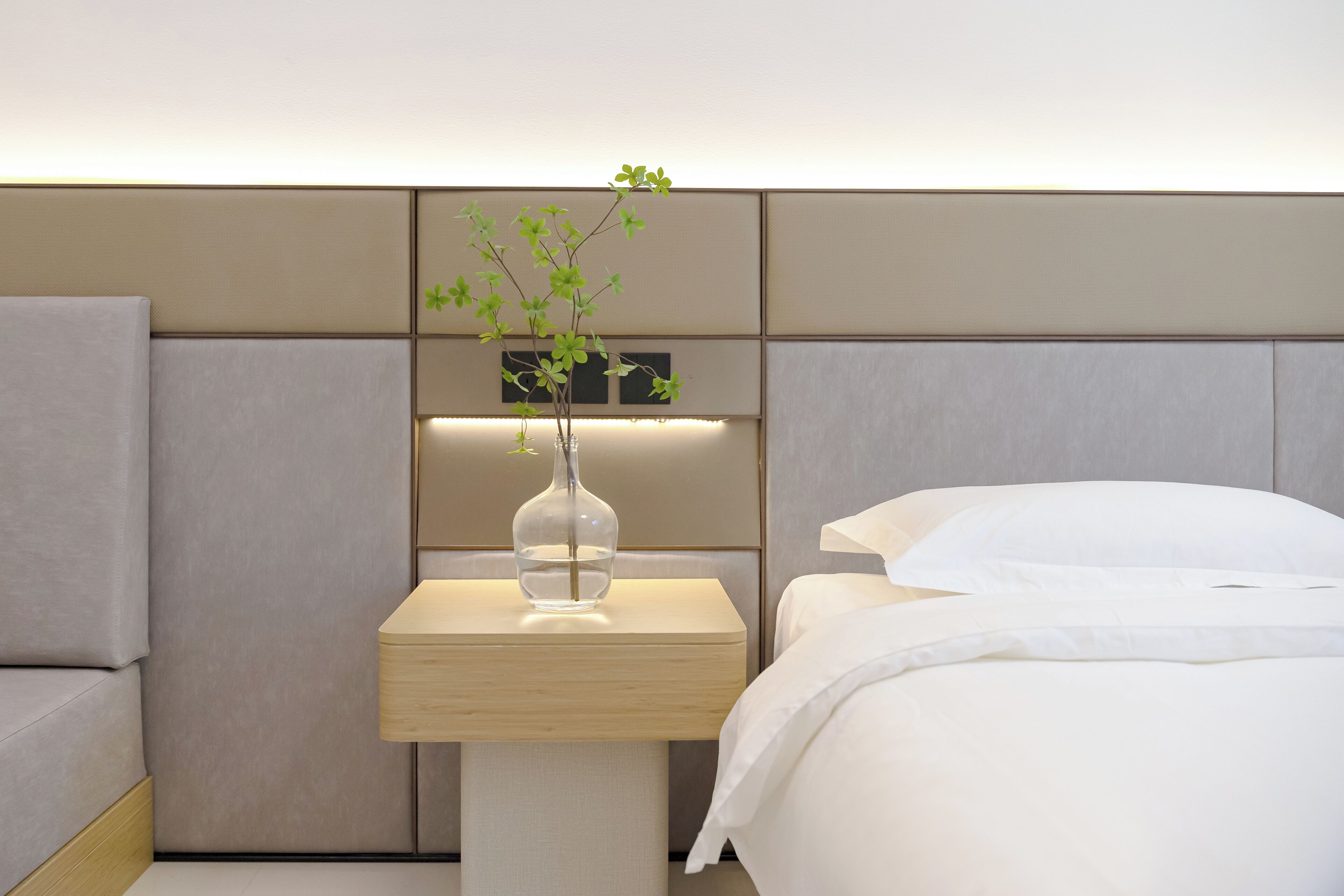 Een moderne hotelkamer met een bed, een nachtkastje met een vaas en een wandpaneel.