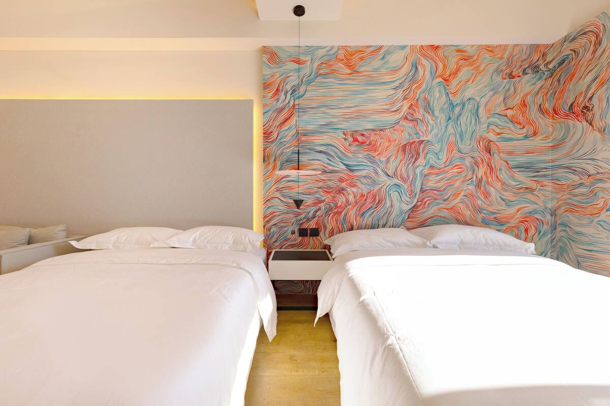 Ett hotellrum med två sängar, en stor, abstrakt väggmålning och en modern lampa.