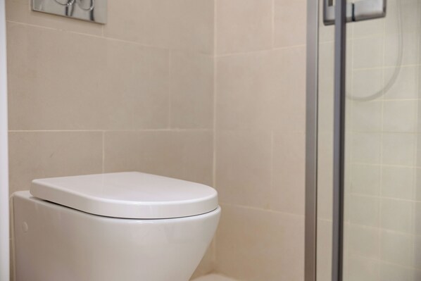 A bathroom with a white toilet, a glass shower enclosure, and beige tiled walls. - Beijing Dream Inn Hotel (Beijing)