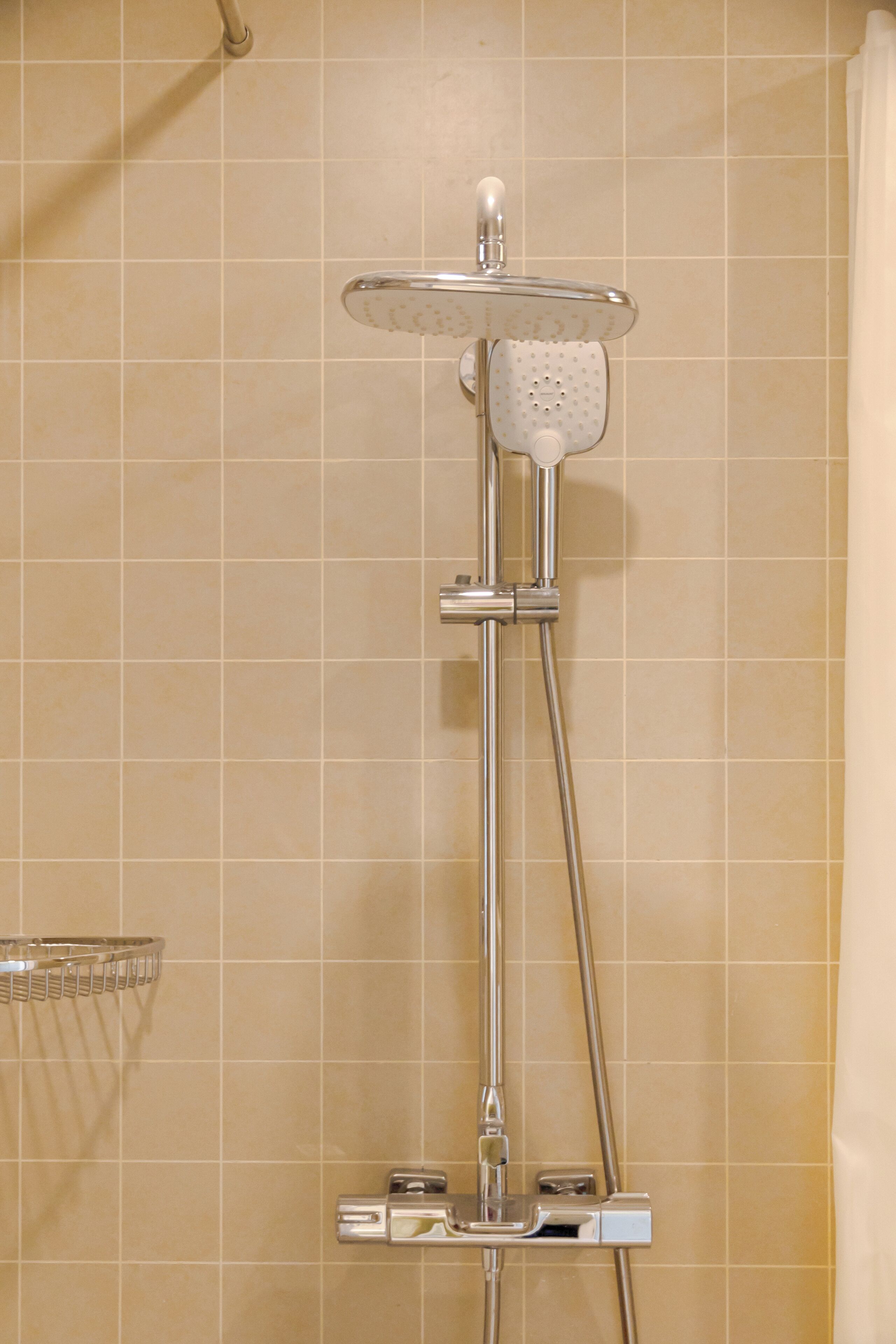 Eine Dusche mit Handbrause und fest installierter Duschköpfe an einer gefliesten Wand.