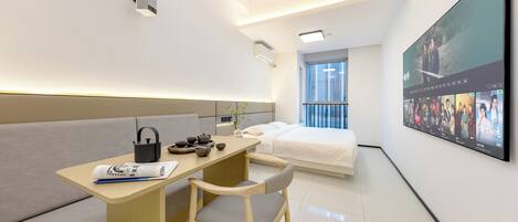 Une chambre d’hôtel moderne équipée d’un canapé, d’un bureau en bois, d’un téléviseur à écran plat et d’une grande fenêtre.