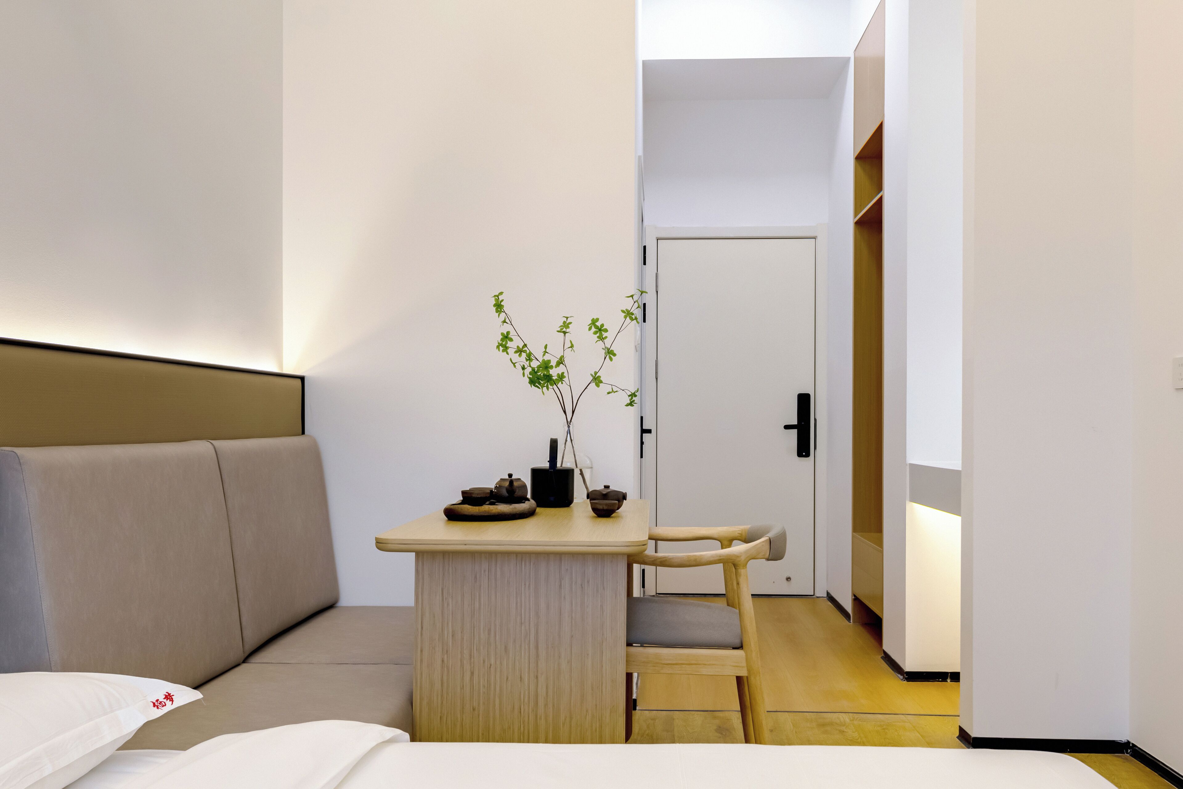 Een kleine hotelkamer met een bed, een bureau met een stoel, een potplant en een kledingkast.