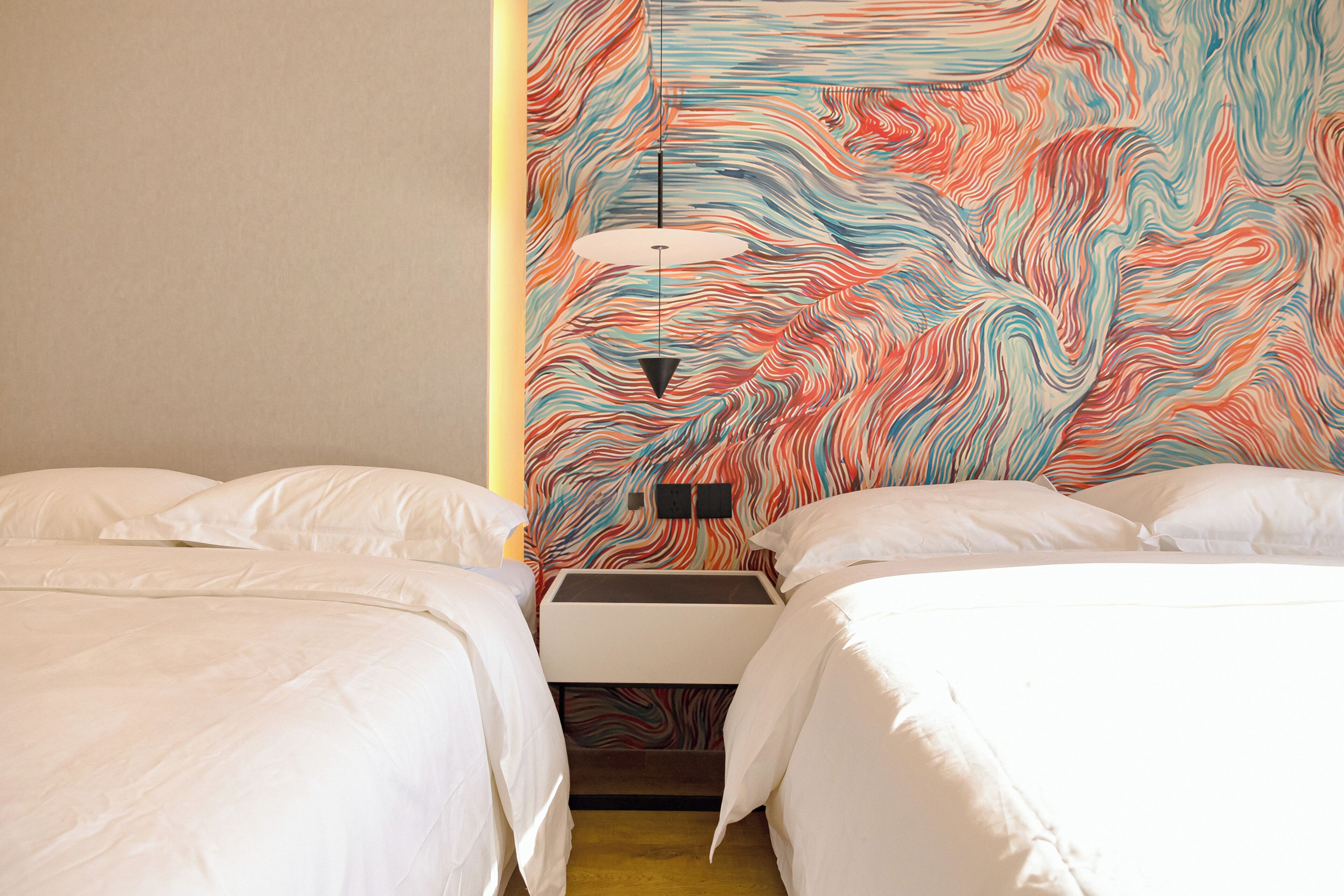A hotel room with two beds, a nightstand, and a colorful abstract wall design.