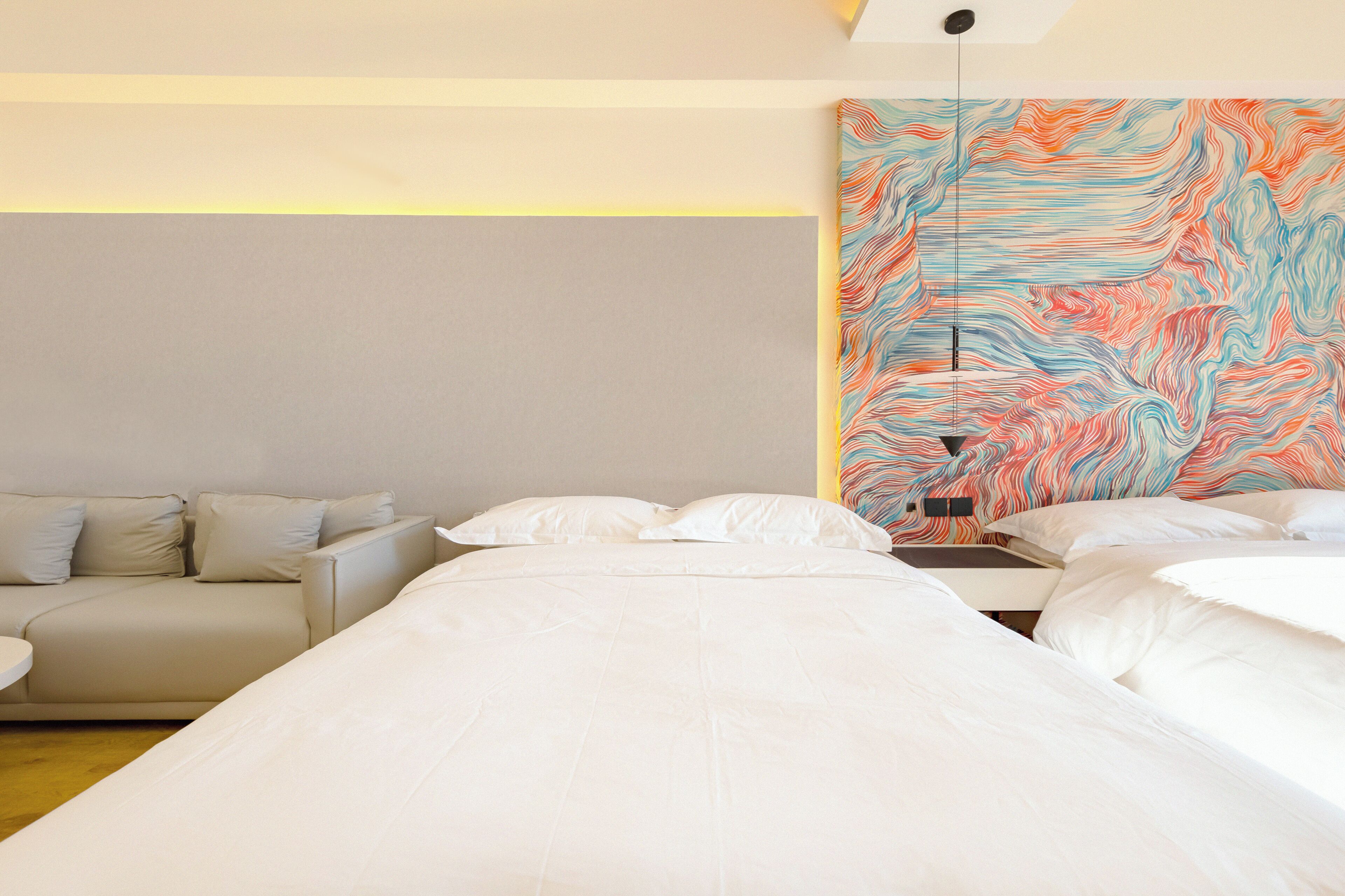 A hotel room with a bed, a sofa, and a colorful abstract painting on the wall.